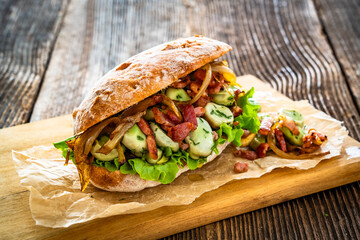 Takeaway sandwich with broad beans, fried bacon and caramelized onion on wooden table