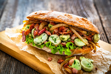 Takeaway sandwich with broad beans, fried bacon and caramelized onion on wooden table