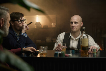 A group of men enjoying time playing poker in a dimly lit bar while sipping on drinks