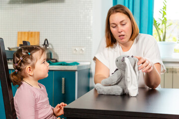 Female teacher or nanny guiding toddler in interactive game in cozy kitchen. Concept of early...