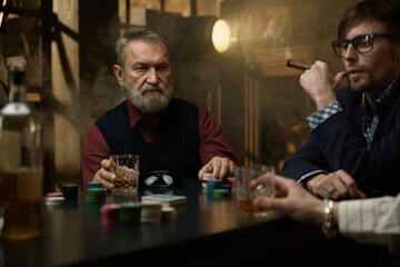 An experienced mature man sits at the poker table enjoying his whiskey and playing with chips