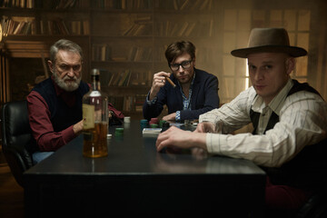 A group of men enjoying time playing poker in a vintage lit bar while sipping on drinks