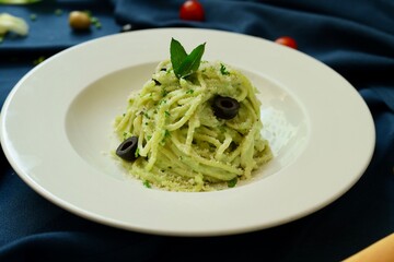 Pesto spaghetti pasta with bread and basil on white plate