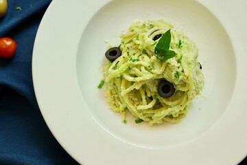 Pesto spaghetti pasta with bread and basil on white plate