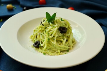 Pesto spaghetti pasta with bread and basil on white plate