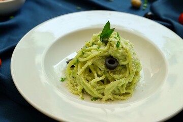 Pesto spaghetti pasta with bread and basil on white plate