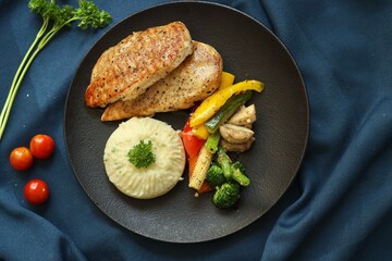 Grilled chicken with vegetables on the side served on a fancy white plate in a restaurant or cafe background 