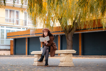 Tranquil weekend scene with a student reading on a city bench in stylish autumn attire. Education...