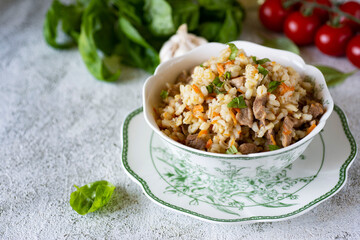 A hearty lunch: pearl barley with meat and vegetables on a beautiful white plate on a light...