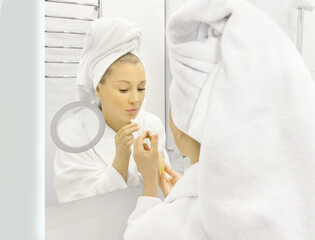 woman looking in the mirror in the bathroom and taking care of her skin.	