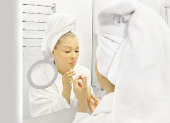 woman looking in the mirror in the bathroom and taking care of her skin.	