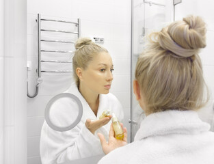 woman looking in the mirror in the bathroom and taking care of her skin.	