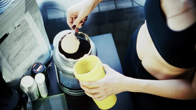 Person scooping protein powder into shaker bottle for fitness