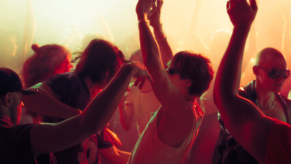 Crowd of people dancing energetically at a music concert with vibrant lighting. Concept of music, concert, party.