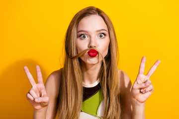 Playful young woman making a quirky mustache pose with her hair and showing peace signs against a...