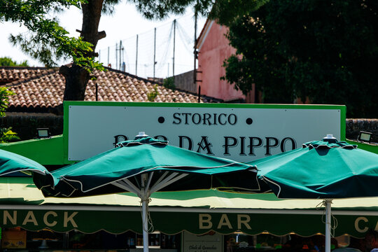 Burano, Italy - June 25, 2025: Historic Bar da Pippo with green umbrellas and vibrant outdoor seating, showcasing Italian cafe culture in a charming street setting