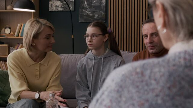 Middle-aged Caucasian parents talking to female psychologist during family therapy session with their teenage daughter turning away avoiding conversation
