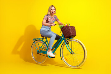 Young woman enjoying a bicycle ride with a basket on a vibrant yellow background exuding energy and...