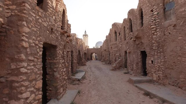 Walking past ruins of Ksar Hadada town in Tunisia, with small mosque in the background
