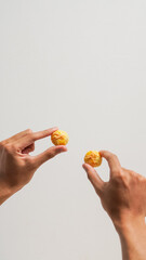 Two hands holding small, round yellow snacks on a clean white background, showcasing bite-sized treats or food items.