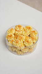 Delicious flower-shaped cookies with sprinkles in a clear plastic container, a sweet festive snack on a bright background.