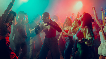 People dancing energetically at a vibrant night club with colorful lights. Concept of nightlife party, youth, summer, festivity, celebration
