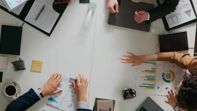 High angle shot of four multiethnic young entrepreneurs discussing business strategy and stacking hands to secure agreement at white desk