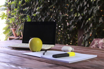 The laptop sits on a wooden table, with a notepad and a pen and bright green marker in the foreground.