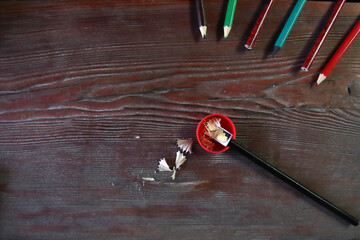 A red pencil sharpener and pencil shavings lie on a wooden table, top view.