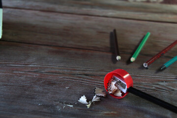 On a wooden table there is a red sharpener and pencil shavings