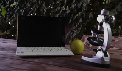 There is a microscope, a laptop, and a green apple on a wooden table. Concept of learning and research