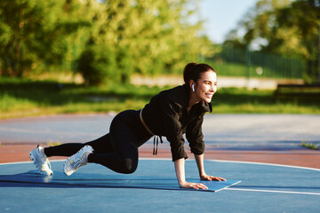 Young sportswoman doing mountain climber exercise on fitness mat outdoors