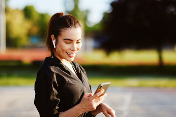 Young sportswoman using smartphone and listening music with wireless earphones