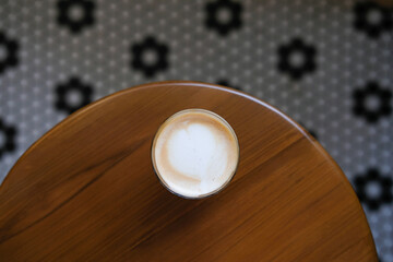 Top view of a cappuccino with beautiful heart latte art, resting on a polished wooden table....