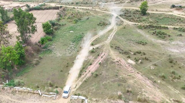 Car moving between farm lands with dust in the back offroad