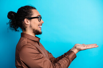 Confident young man in brown shirt and glasses presenting with an open hand gesture against a...