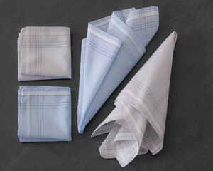 Folded blue and beige handkerchiefs arranged on a dark background, showcasing classic men's accessories in a clean, elegant style.