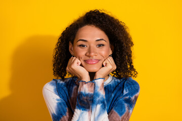 Cheerful young woman with curly hair poses against a bright yellow backdrop, embracing vibrant...
