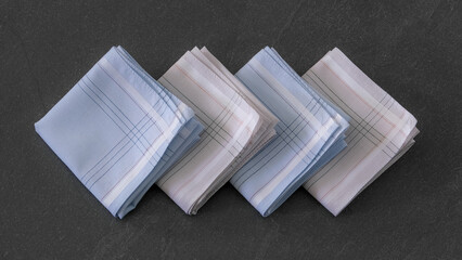 Folded blue and beige handkerchiefs arranged on a dark background, showcasing classic men's accessories in a clean, elegant style.