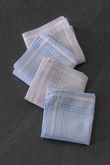 Folded blue and beige handkerchiefs arranged on a dark background, showcasing classic men's accessories in a clean, elegant style.