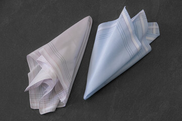 Folded blue and beige handkerchiefs arranged on a dark background, showcasing classic men's...
