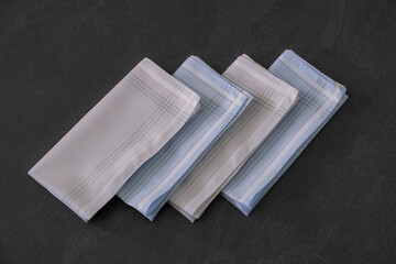 Folded blue and beige handkerchiefs arranged on a dark background, showcasing classic men's accessories in a clean, elegant style.