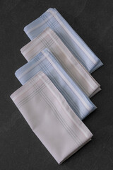 Folded blue and beige handkerchiefs arranged on a dark background, showcasing classic men's...