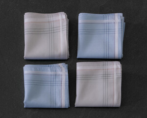Folded blue and beige handkerchiefs arranged on a dark background, showcasing classic men's accessories in a clean, elegant style.