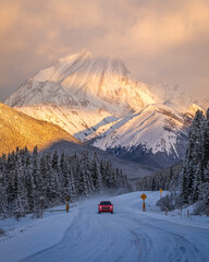 Red car driving on snowy road at sunrise in Kananaskis Country