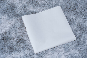 Minimalistic newspaper mockup with blank folded paper lying on a fluffy gray carpet. Layout for showcasing print layout and editorial design.