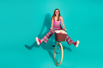 Cheerful young woman on retro bicycle with flower basket enjoying fun moments against bright...