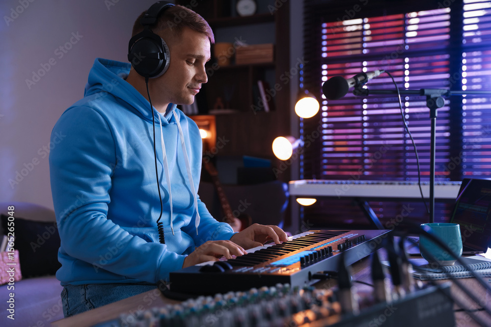 Poster man in headphones working with midi keyboard at table in home studio