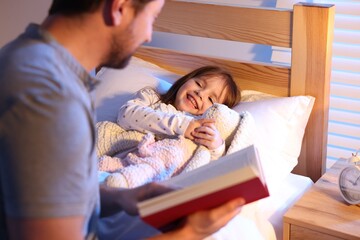 Father reading bedtime story to his happy daughter at home, selective focus