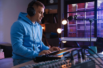 Man in headphones working with MIDI keyboard at table in home studio